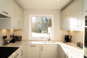 Una cocina moderna con armarios blancos, una ventana con vistas a árboles, un fregadero y una cafetera.
