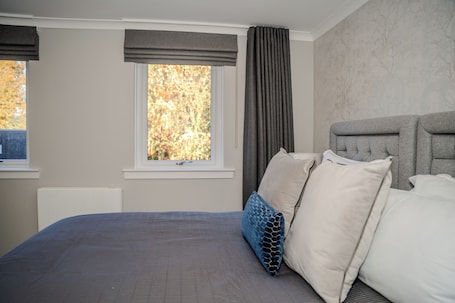 A bedroom with a bed, a window with curtains, a radiator, and a wall with a tree pattern.. 55 Guthrie - Gleneagles Village