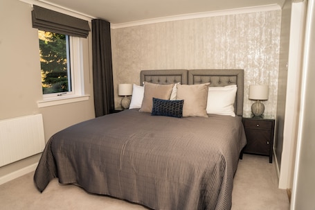 A bedroom with a large bed, two bedside tables, a window with curtains, and a radiator.. 55 Guthrie - Gleneagles Village