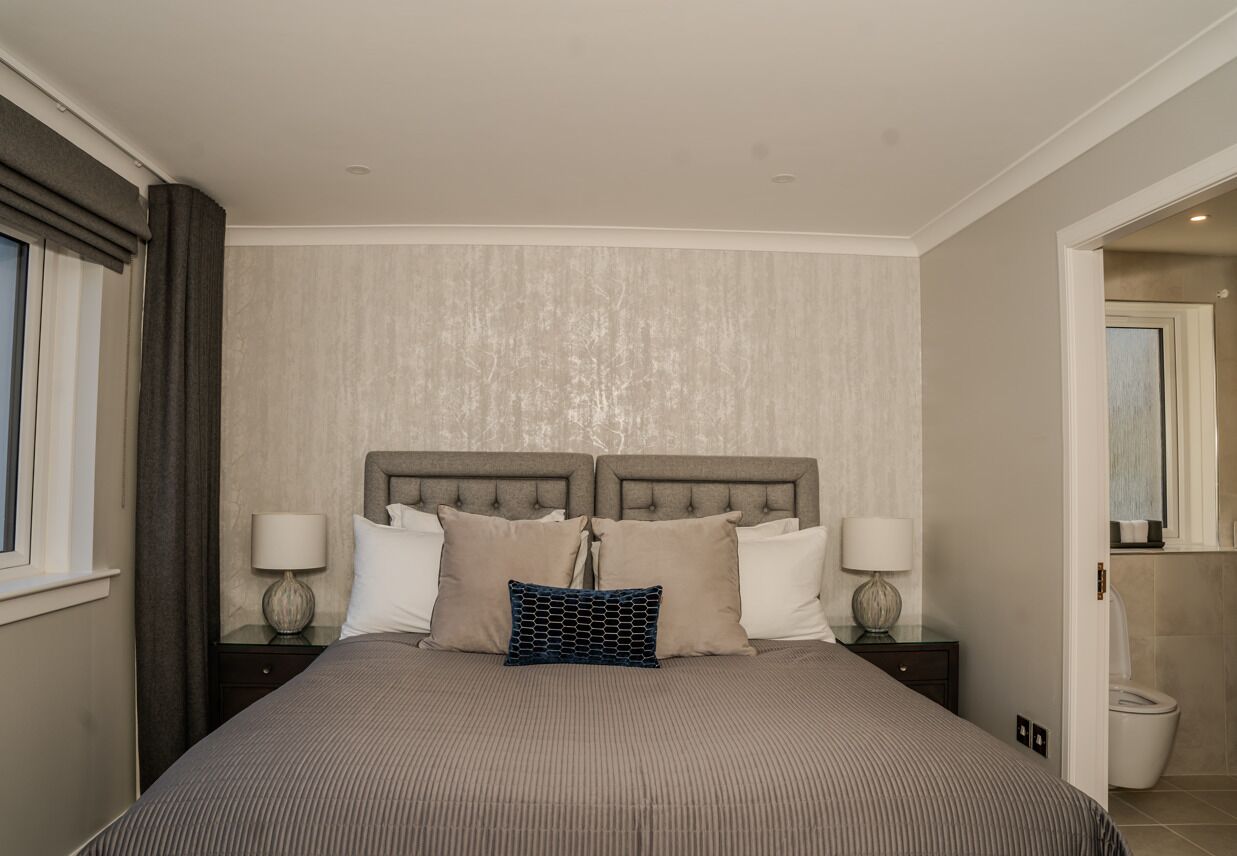 A bedroom with a large bed, two bedside tables with lamps, a headboard, and a window with curtains.