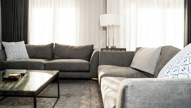 A modern living room with a grey sofa, a glass coffee table, a floor lamp, and sheer curtains. - 55 Guthrie - Gleneagles Village (Gleneagles Village)