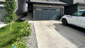 Une maison à deux étages avec un garage, une allée et une voiture blanche garée dans l’allée.