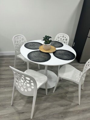 Una mesa redonda con una planta en maceta, rodeada de sillas blancas con abertura circular.