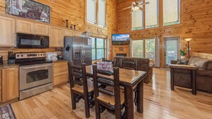 A cabin interior with wooden walls, a dining area, kitchen with appliances, and a ceiling fan. - I Love View Too (Gatlinburg)