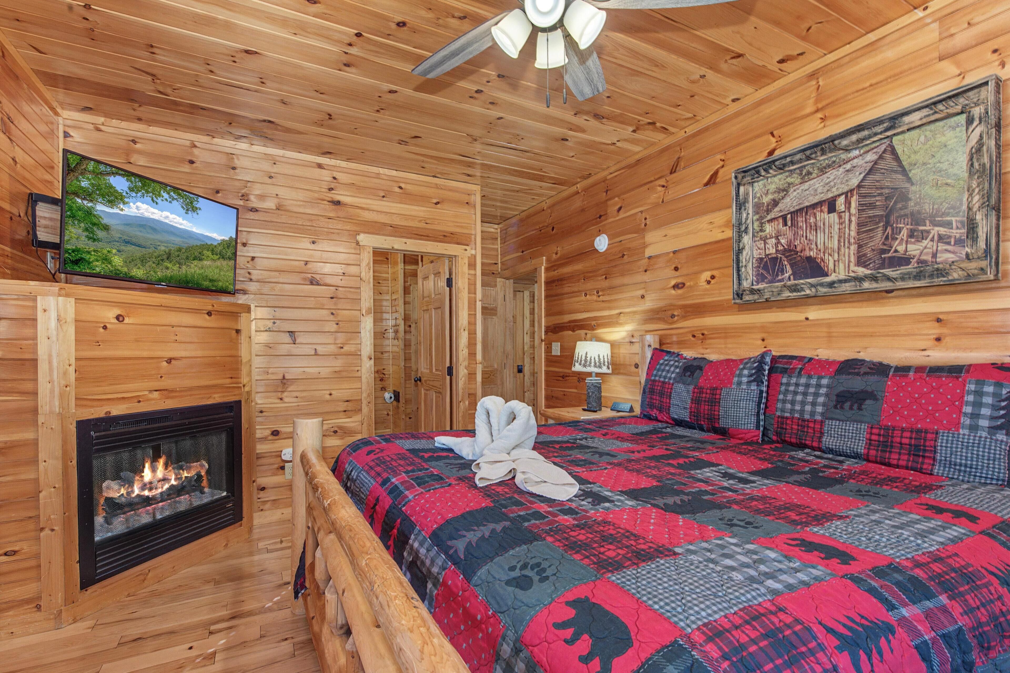 Una habitación de cabaña de madera con chimenea, televisor, cama con colcha y un cuadro en la pared.