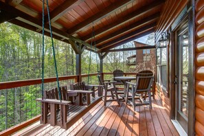 A wooden deck with outdoor seating, a view of a forest, and a cabin structure. - I Love View Too (Gatlinburg)