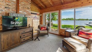 A cozy room with a television, wicker furniture, and a large window overlooking a lake. - Granite Lake Retreat w/ Private Dock (Annandale)