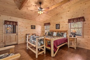 A wooden cabin bedroom with a bed, a wooden chair, a nightstand, a ceiling fan, and two windows with curtains. - Key to Heaven (Gatlinburg)