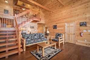 Un interior de madera con una escalera, un sofá, una mesa de centro y una chimenea.