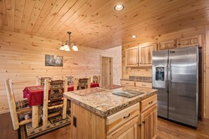 Interior de una cabaña de madera con cocina, mesa de comedor de madera y sillas, y un refrigerador.
