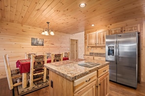 A wooden cabin interior with a kitchen area, wooden dining table with chairs, and a refrigerator. - Key to Heaven (Gatlinburg)