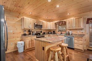 A wooden-paneled kitchen with a central island, stainless steel appliances, and wooden stools. - Key to Heaven (Gatlinburg)