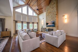 A spacious living room with a high ceiling, stone fireplace, and large windows. - Spacious 5-bedroom lake front house in Kingsland with game room (Kingsland)