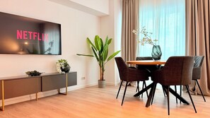 Una sala moderna con un televisor de pantalla plana, una mesa de comedor con sillas, una planta en maceta y un florero con flores.