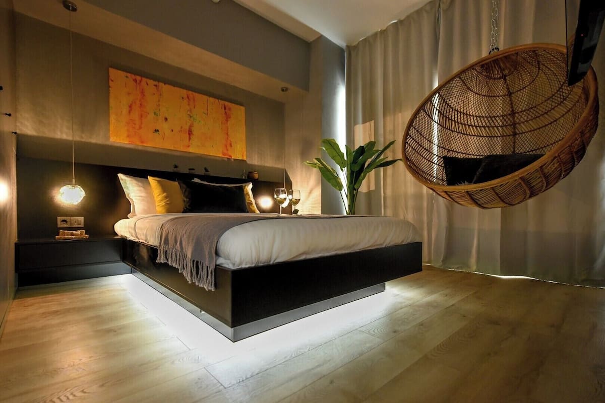A modern bedroom with a bed, bedside tables, a hanging chair, and a large window.
