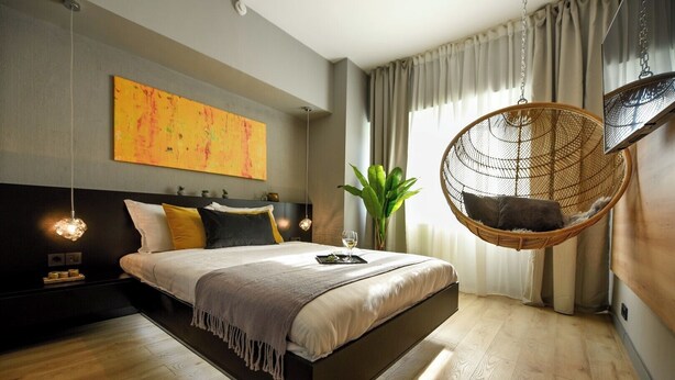 Une chambre moderne avec un fauteuil suspendu, un grand lit et une plante.