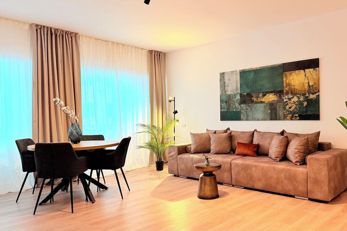 A modern living room with a sofa, a dining table with chairs, a floor lamp, and a large abstract painting on the wall.
