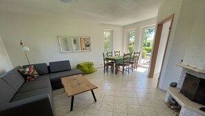 Een woonkamer met een bank, een salontafel, een open haard en een eethoek met stoelen en een tafel.