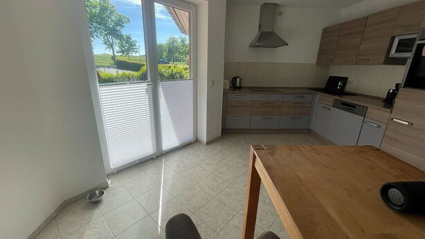 Een moderne keuken met een houten tafel, een inbouwoven en uitzicht door grote schuifdeuren.