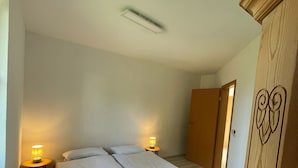Een slaapkamer met een bed, bedlampen, een kledingkast en een deur die naar een andere kamer leidt.