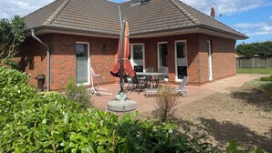 Een tweelaags bakstenen huis met een terras, tuinmeubilair en een schotelantenne.