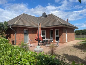 Ein zweistöckiges Backsteinhhaus mit einer Terrasse, Gartenmöbeln und einer Sat-Schüssel.