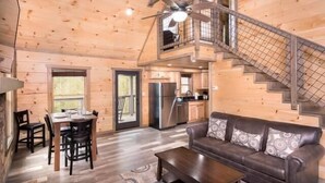 Ein Holzblockhaus im Inneren mit Essbereich, einer Couch, einer Treppe und einer Küche.