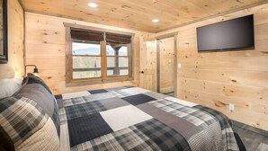 Ein Schlafzimmer einer Holzhütte mit Bett, Fenster, Tür und einem Wand-Fernseher.