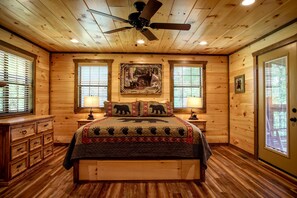 A wooden cabin bedroom with a bed, two nightstands, a ceiling fan, and a window with blinds. - Scenic Solitude (Sevierville)