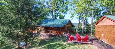 Une cabane dotée d’un toit végétalisé, entourée d’arbres, et une terrasse avec des chaises rouges.