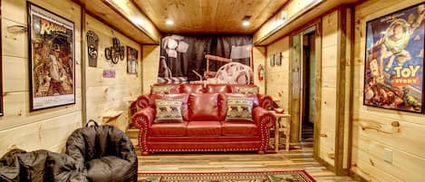 A log cabin interior with a red leather sofa, a black bean bag, and a patterned rug.