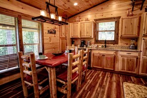 A wooden interior with a dining table, chairs, and a kitchen area with wooden cabinets and a countertop. - Scenic Solitude (Sevierville)