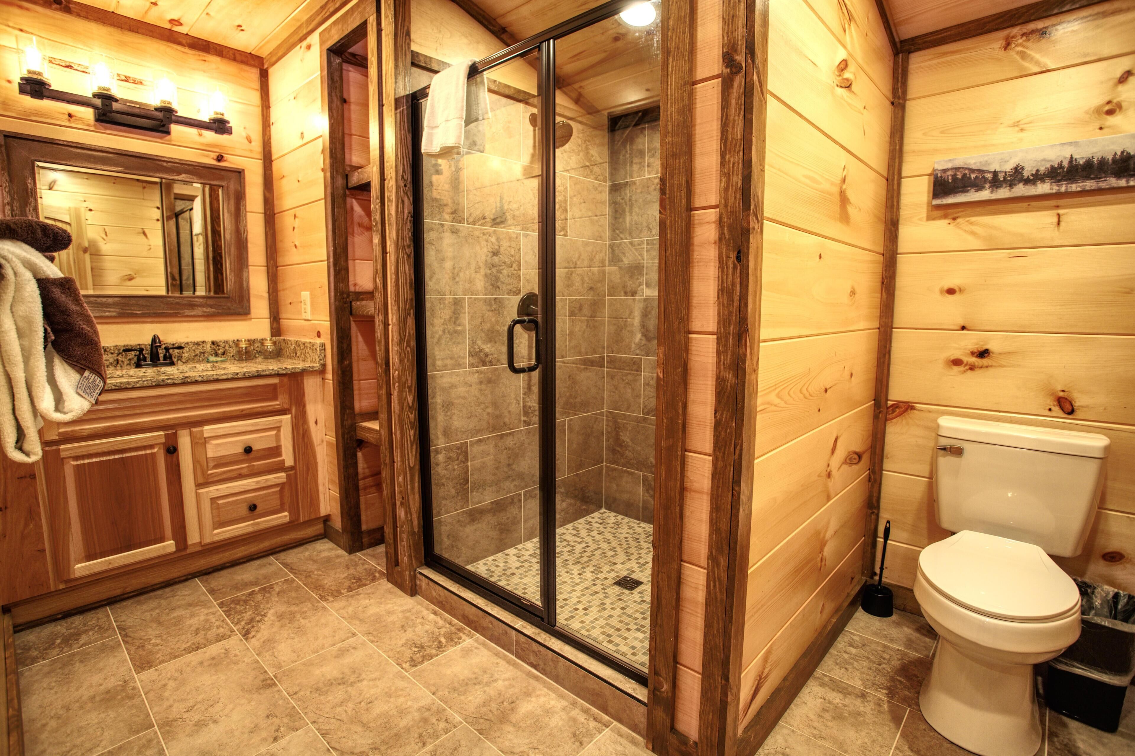 Une salle de bain rustique, avec des murs en bois, comprenant une douche à parois de verre, un lavabo avec un miroir et des toilettes.