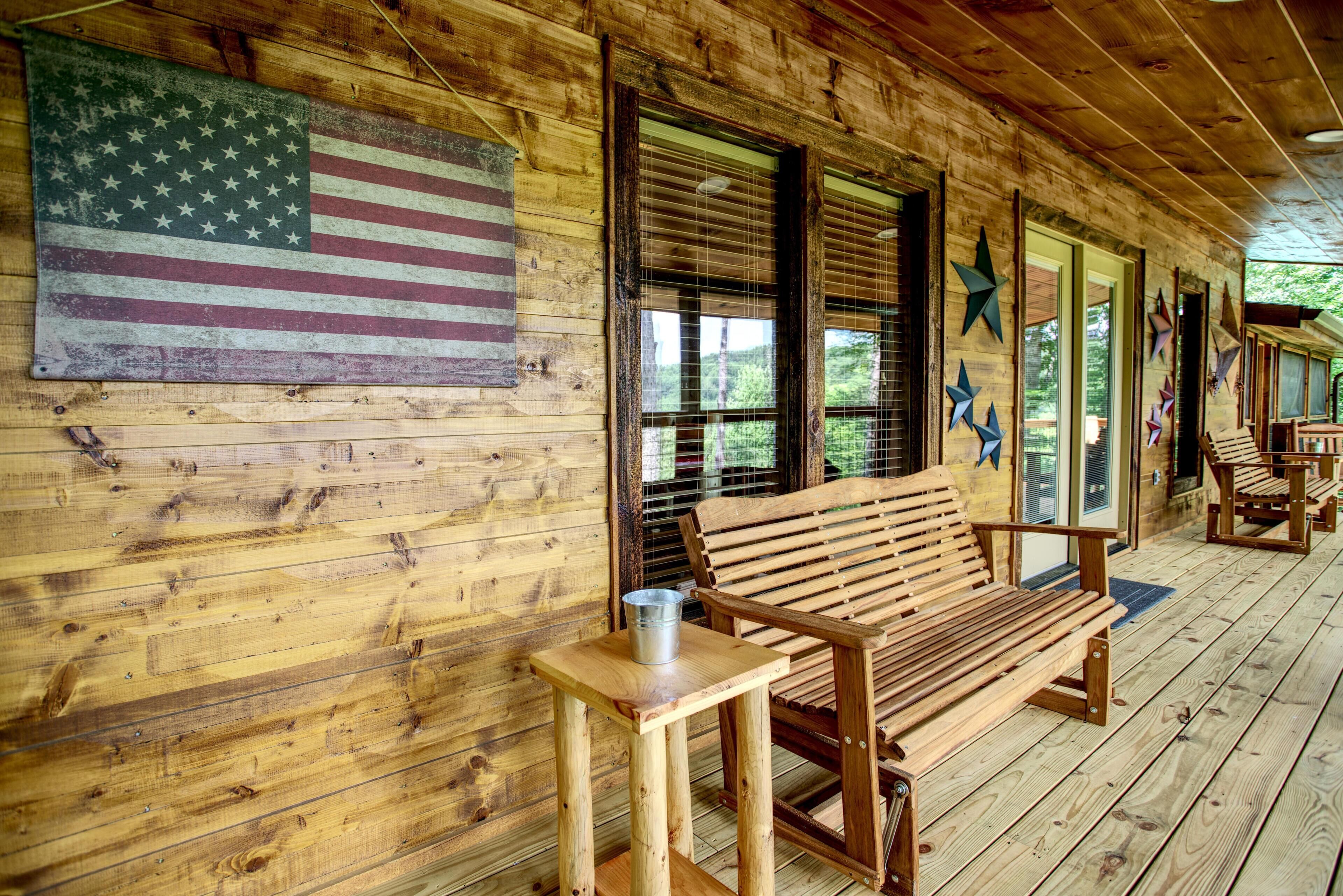 Una cabana de fusta amb una banca de fusta, un cubell metàl·lic i una gran bandera dels Estats Units a la paret.