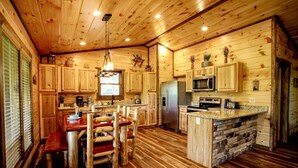 Interior de una cabaña de madera con cocina, comedor y una isla de piedra.