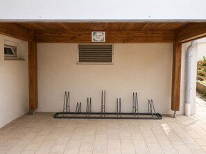 Un espace extérieur abrité, doté d’un plafond en bois, d’une fenêtre avec des lamelles horizontales et d’une étagère en métal sur laquelle sont disposés plusieurs objets.
