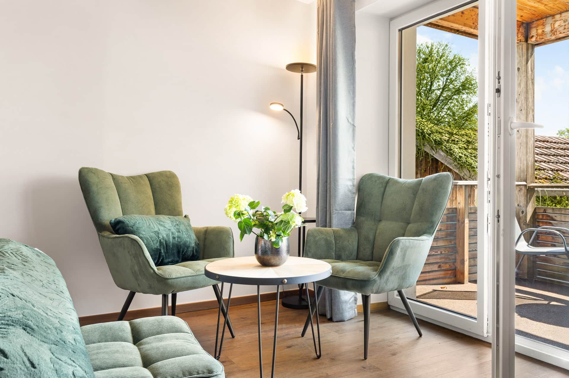 Un salon moderne avec deux fauteuils verts, une table basse ronde et un lampadaire.