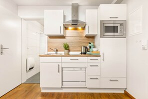Uma cozinha moderna com armários brancos, um exaustor de aço inoxidável, um micro-ondas LG e um forno embutido.