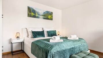 Ein Schlafzimmer mit Bett, Kissen, einem Nachttisch, einer Lampe, einer Bank und einem Bild an der Wand.