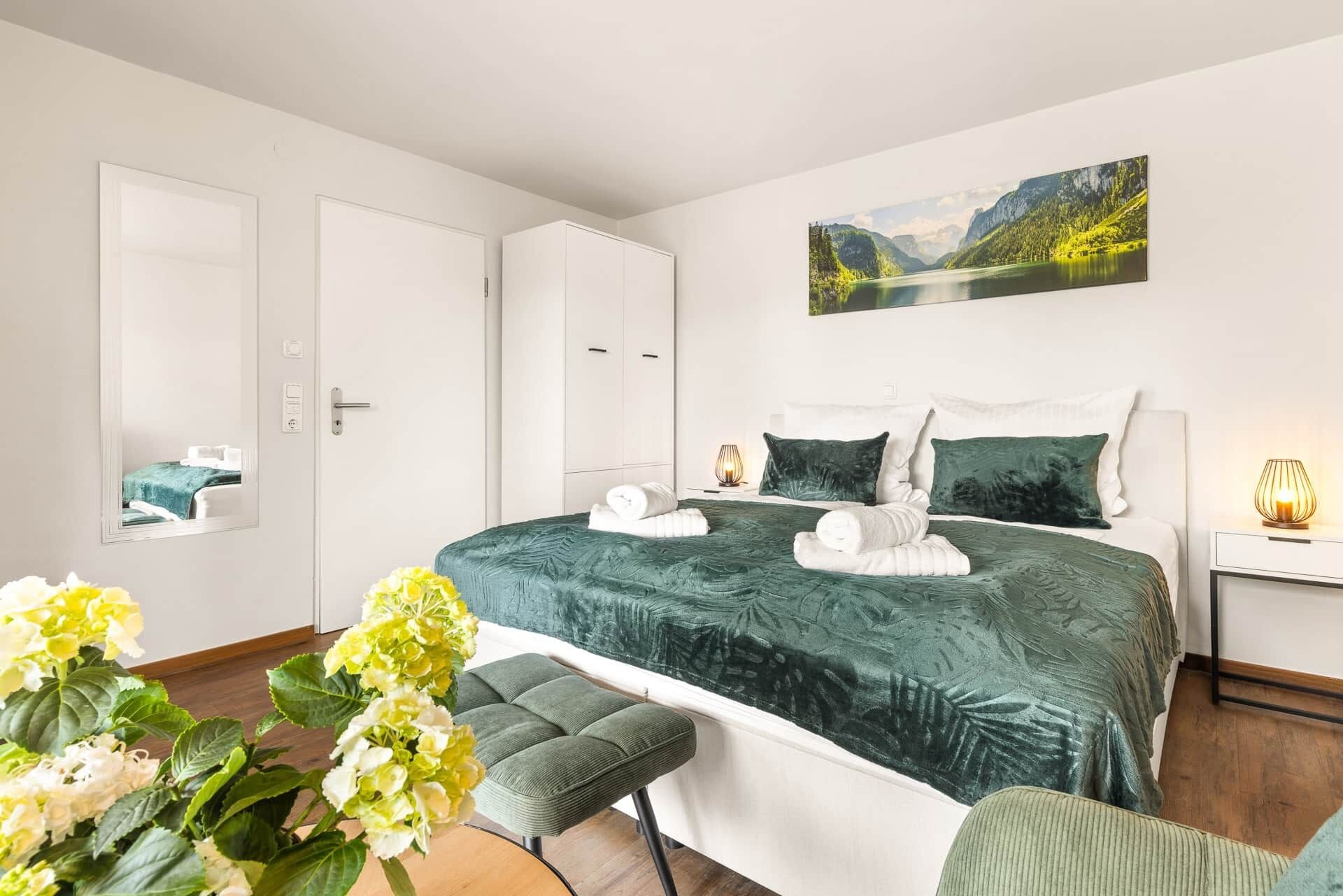 Ein Schlafzimmer mit einem Bett, einem Nachttisch, einer Lampe, einem Sessel und einem Gemälde an der Wand.