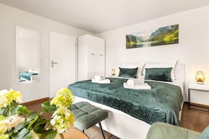 Een slaapkamer met een bed, nachtkastje, lamp, stoel en een schilderij aan de muur.