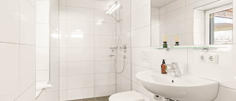 A modern bathroom with white tiles, a toilet, a sink, a shower, and a mirror.