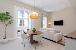 A modern living room with a dining table, chairs, a sofa, a TV, and a large window. - Charming 1bedroom Apt in Granada San Anton 201 (Granada)