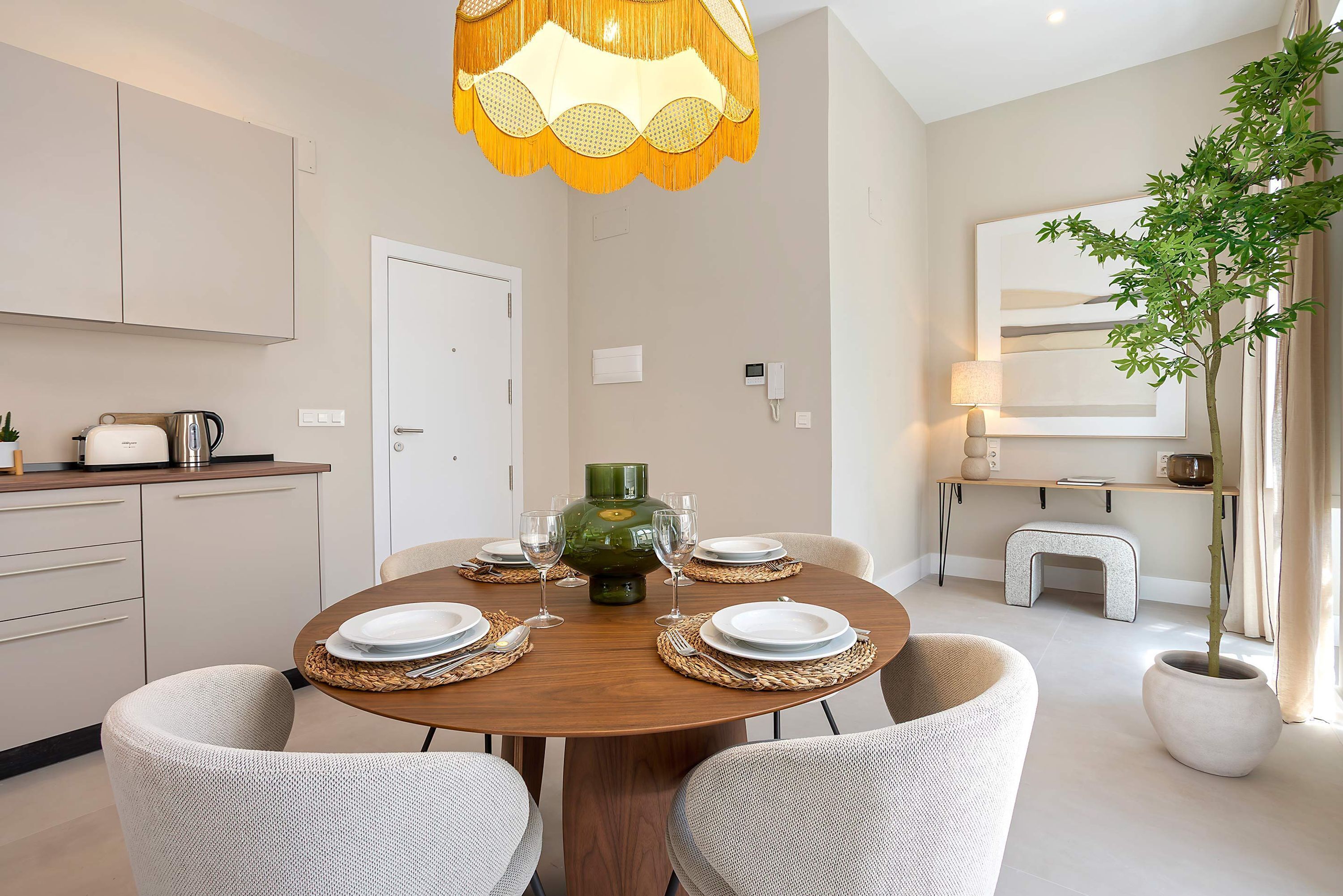 Een eethoek met een ronde tafel, stoelen, een groene vaas en een hanglamp.