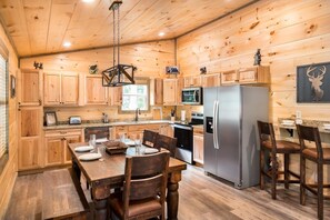 A wooden cabin interior with a kitchen, dining table, chairs, and a refrigerator. - Tennessee Tranquility (Sevierville)