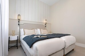 Ein ordentlich eingerichtetes Schlafzimmer mit Bett, Nachttisch, Lampe und Wandleuchte.