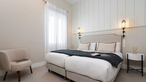 Ein Schlafzimmer mit einem Bett, Nachttischen, einem Sessel und einem Fenster mit Vorhängen.