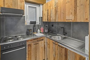 A modern kitchen with a gas stove, oven, stainless steel sink, and wooden cabinets.
