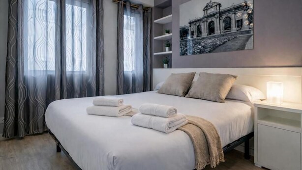 A neatly made bed with towels, a bedside lamp, and a framed picture on the wall. - Plaza de Castilla II (Madrid)