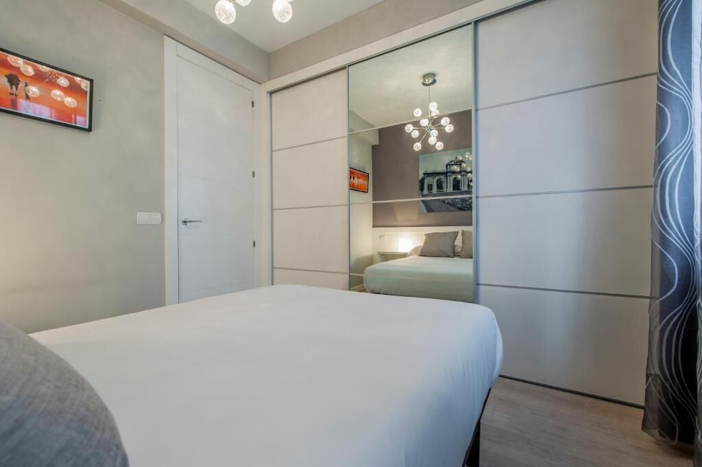Ein Schlafzimmer mit einem Bett, einem Kleiderschrank, einem Spiegel und einer Wandleuchte.